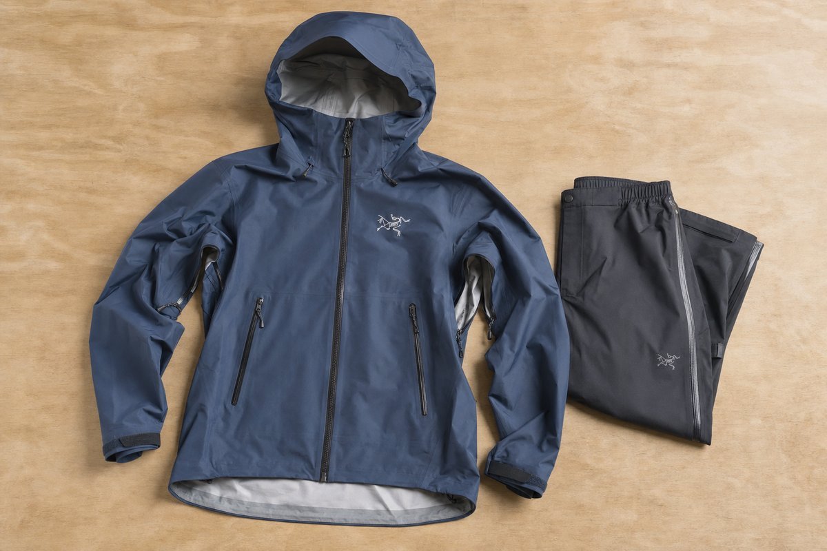 Waterproof rain jacket with hood laid flat showing sealed seams and ventilation zippers, with rain pants folded beside it